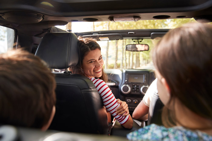Family enjoying a cheerful car ride together, with a woman smiling back at passengers from the front seat